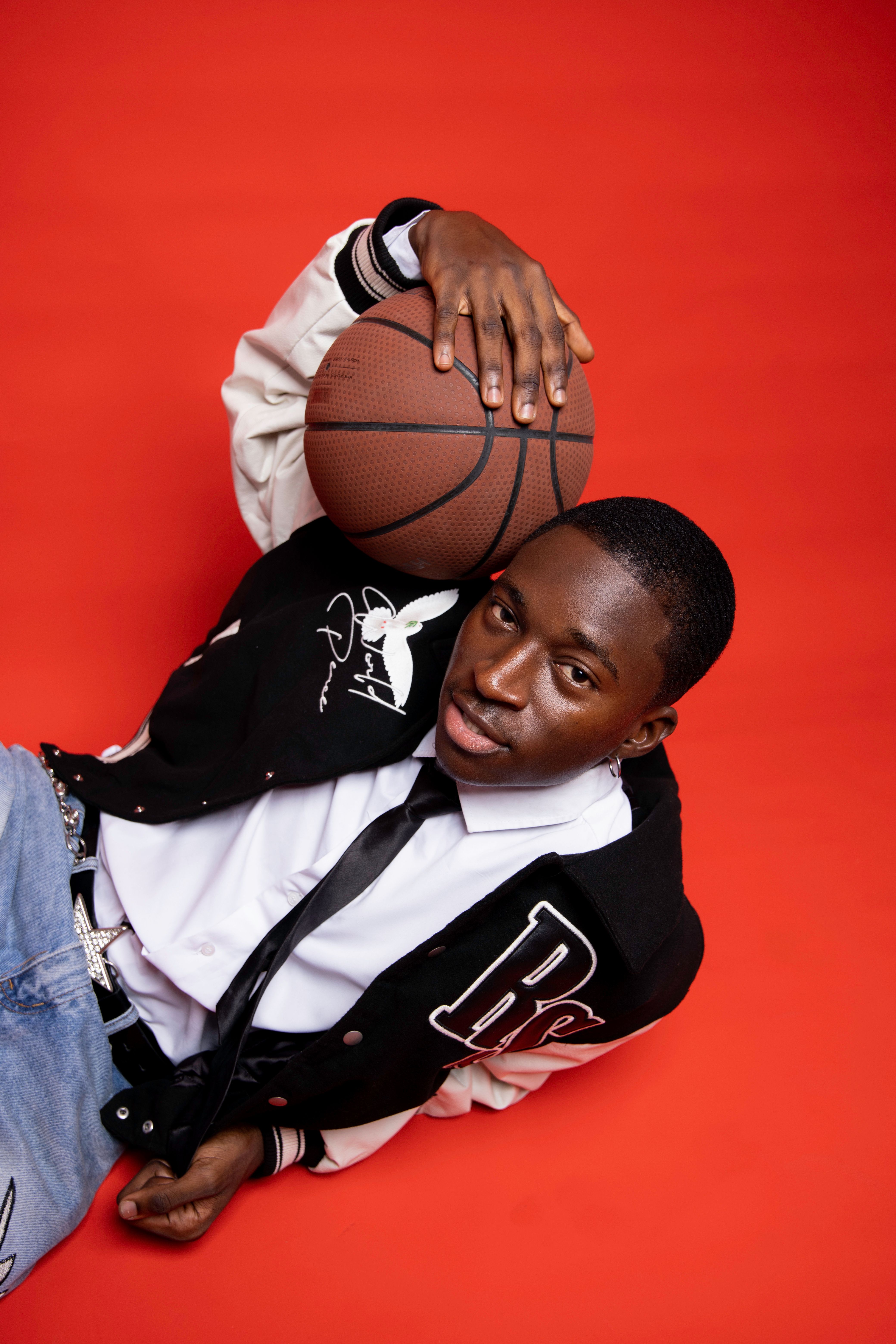 Young man holding basketball on a bright red background. Stylish and athletic theme.