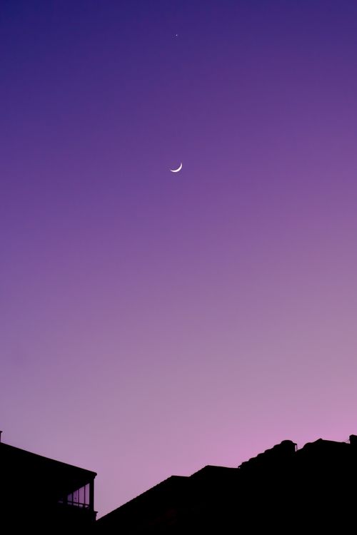 Free Silhouette of urban buildings against a twilight sky with a crescent moon. Stock Photo