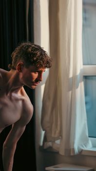 Artistic portrait of a man bathed in warm sunlight near a window indoors.