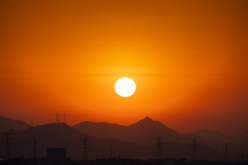 Free Captivating sunset with mountains and electrical towers silhouetted against an orange sky. Stock Photo