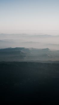 A tranquil aerial shot capturing mist-covered mountains under a clear sky.