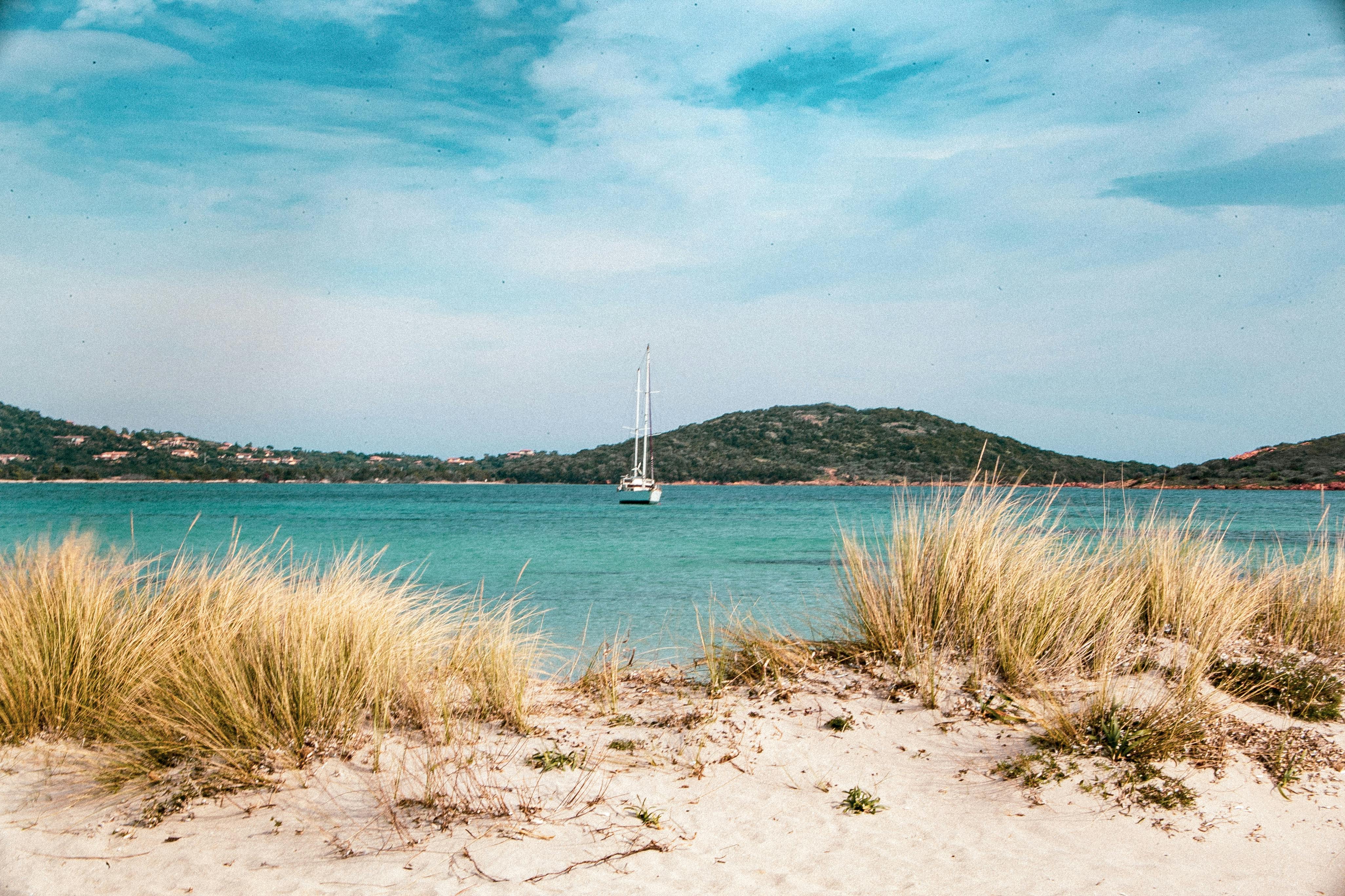 Serene view of a sailboat on the turquoise waters, framed by sandy dunes in France.