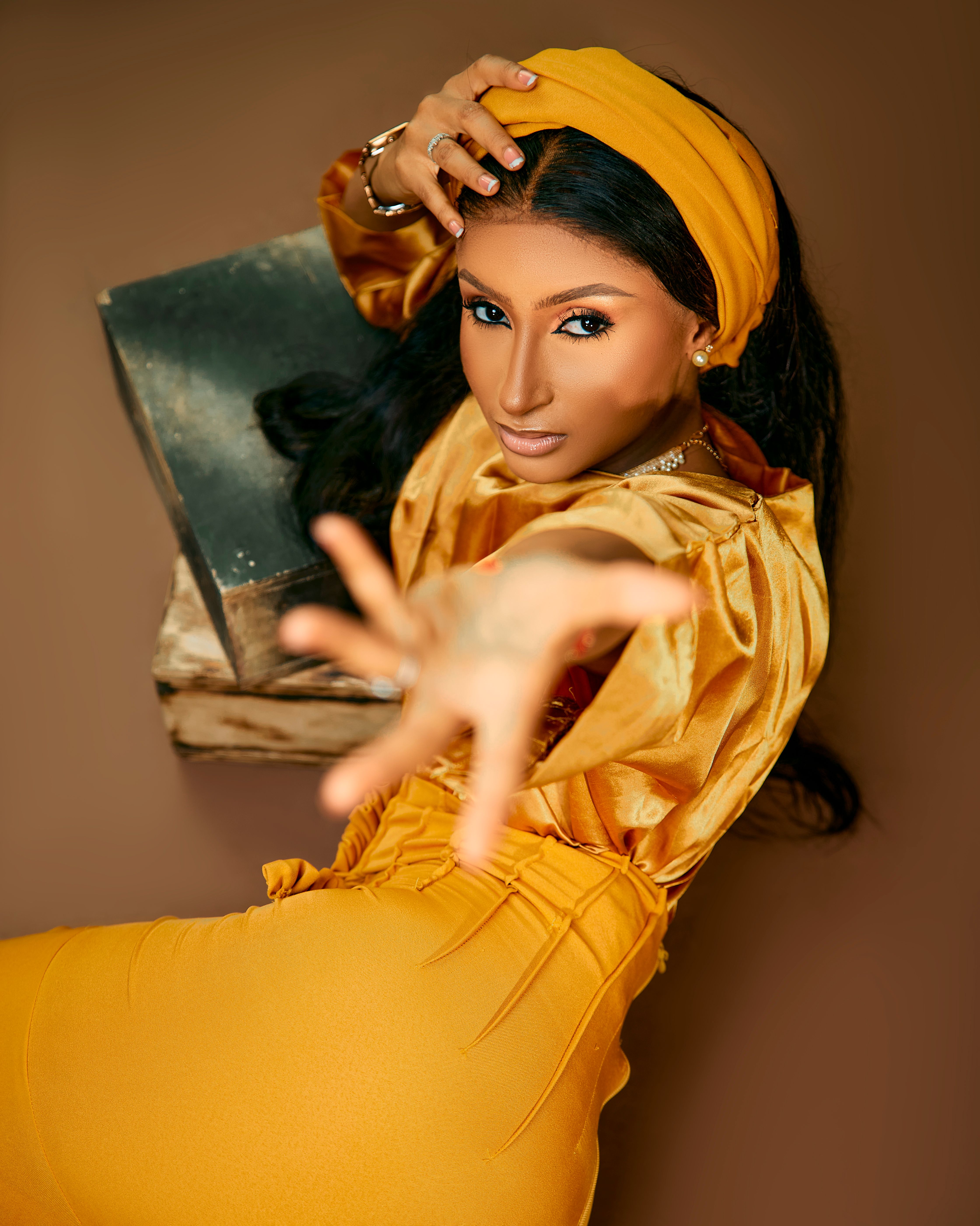 Creative portrait of a woman in vibrant yellow outfit reaching towards the camera with a dynamic pose.