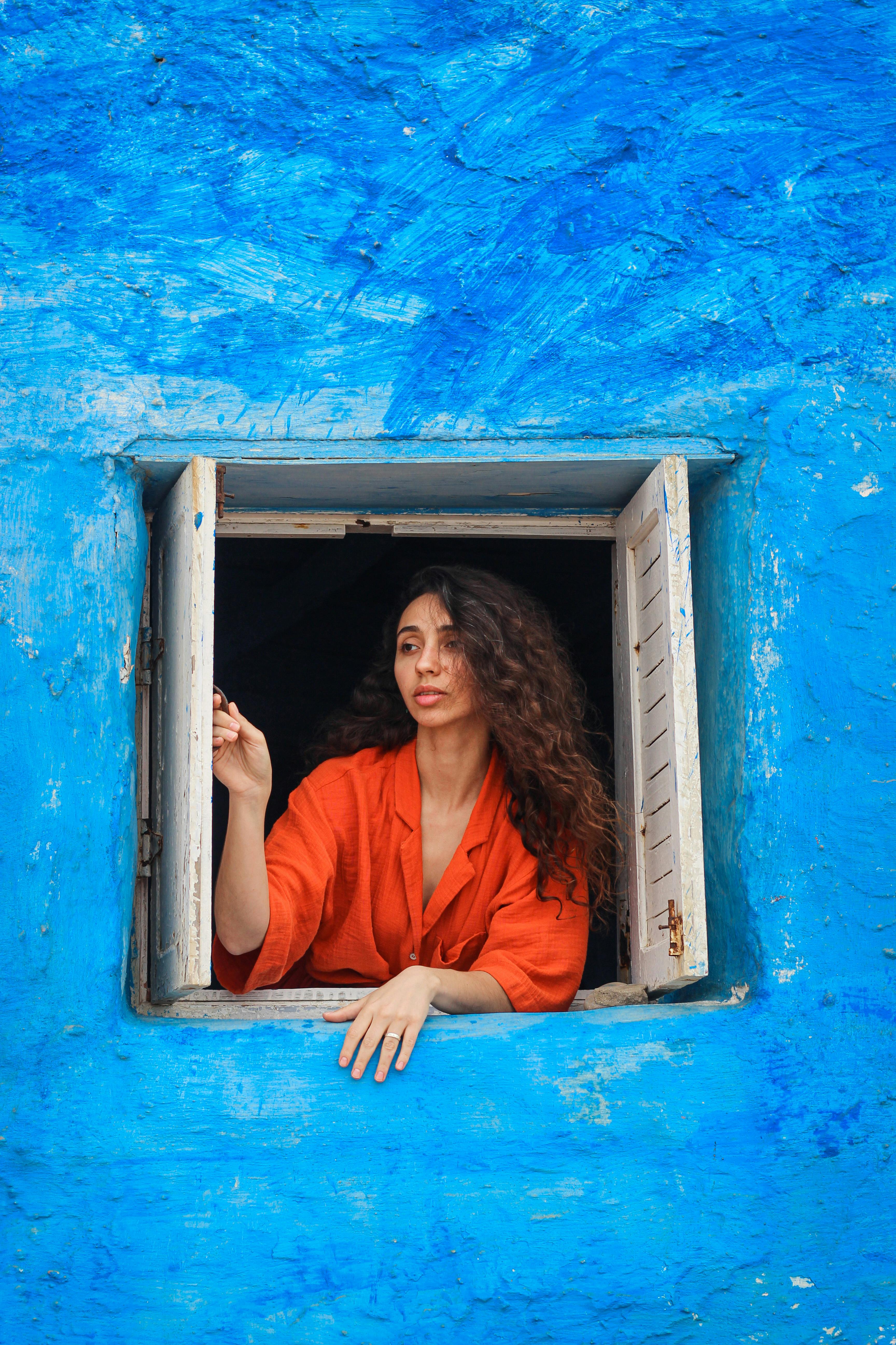 Woman in orange shirt posing in a vibrant blue window, creating a vivid contrast.
