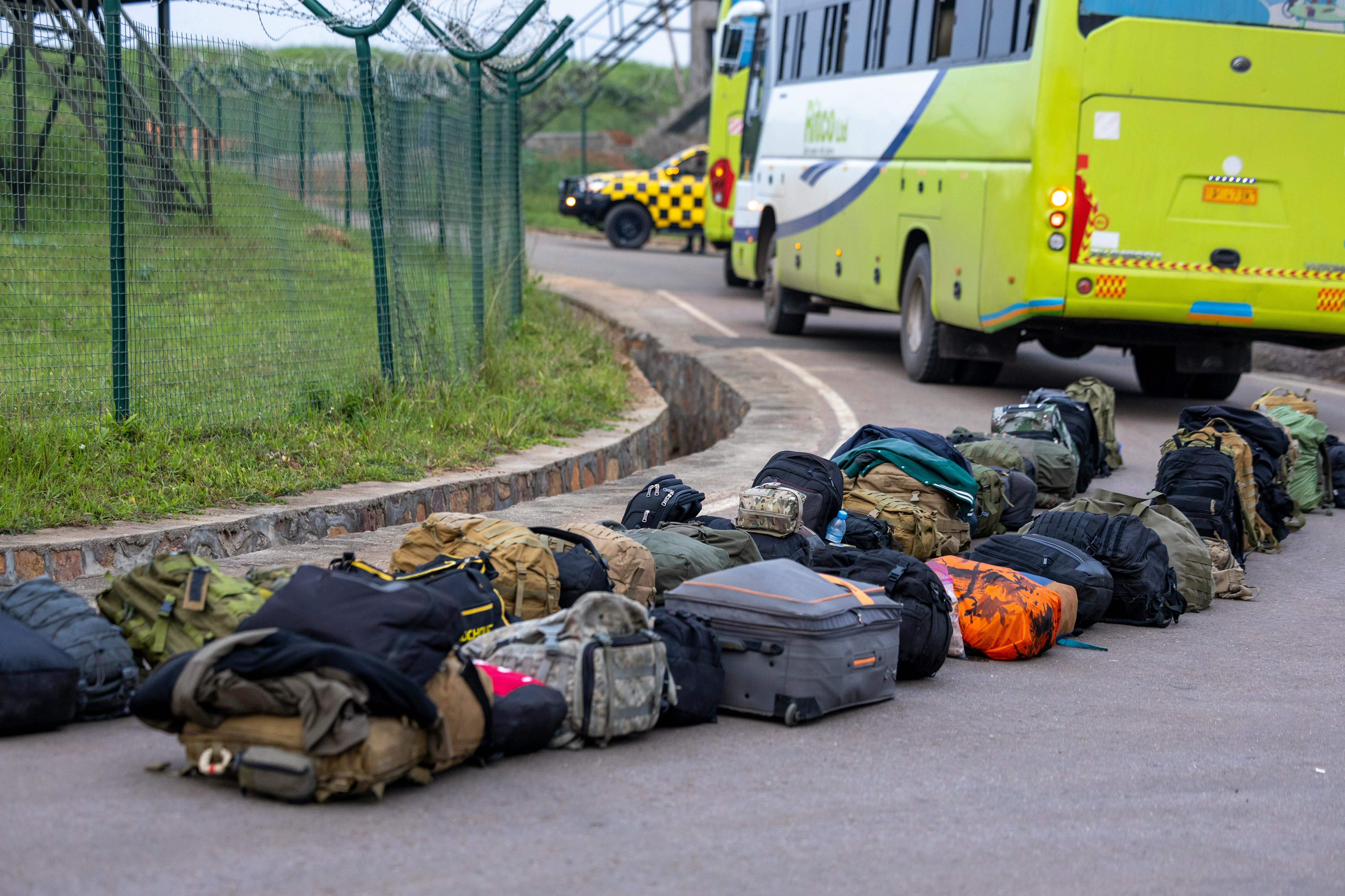A row of backpacks and luggage near a green bus on a roadway.