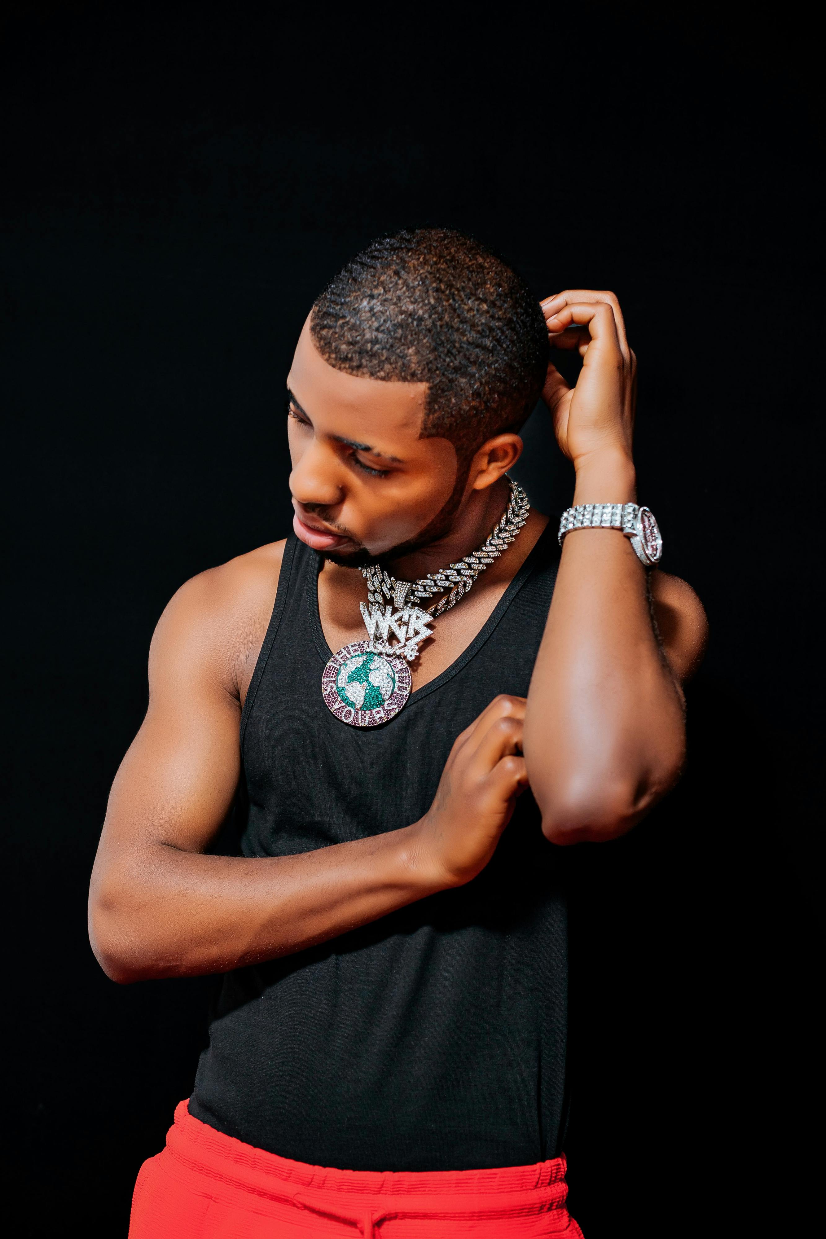 A fashionable young man poses confidently, wearing distinctive jewelry and a black tank top.