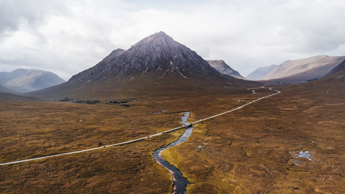 Drum și râu prin valea Glencoe din Scoția, sub silueta muntelui Buachaille Etive Mòr
