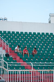 A minimalistic view of three young people sitting in empty stadium seats.
