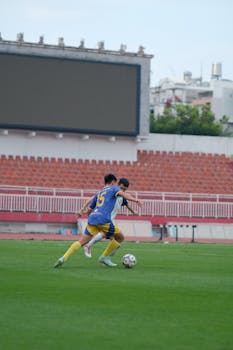 Two soccer players in motion on a grassy stadium field during the day.