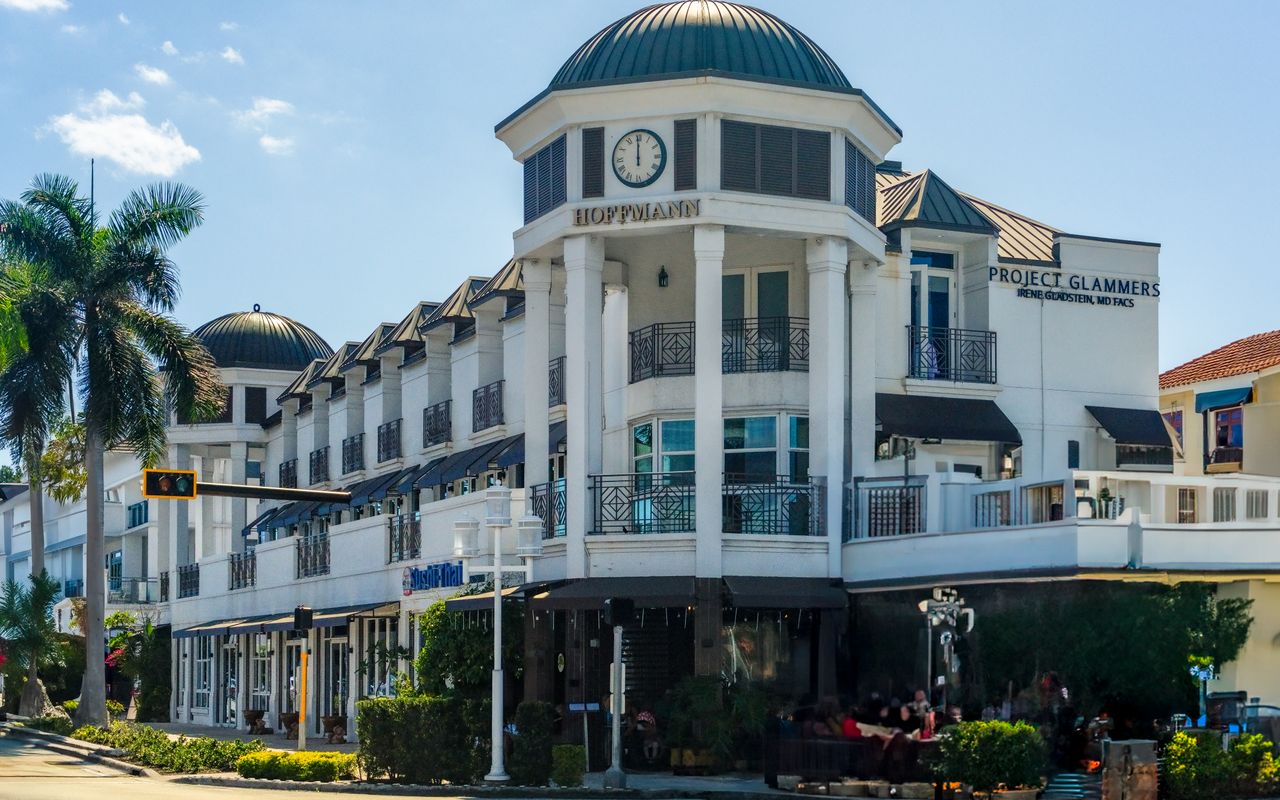 Elegant architecture at a shopping center in Naples, Florida with palm trees and clear skies.