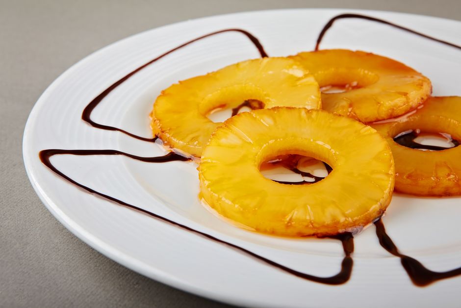 Delicious caramelized pineapple rings served on a white plate with chocolate drizzle.
