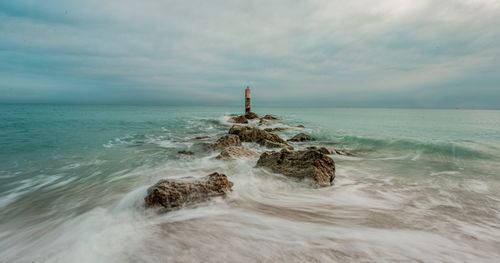 Free Peaceful ocean view with rocks leading into the water, under a cloudy sky. Stock Photo