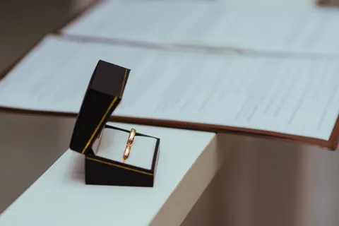 Pair of wedding rings in an open black box on a table beside papers