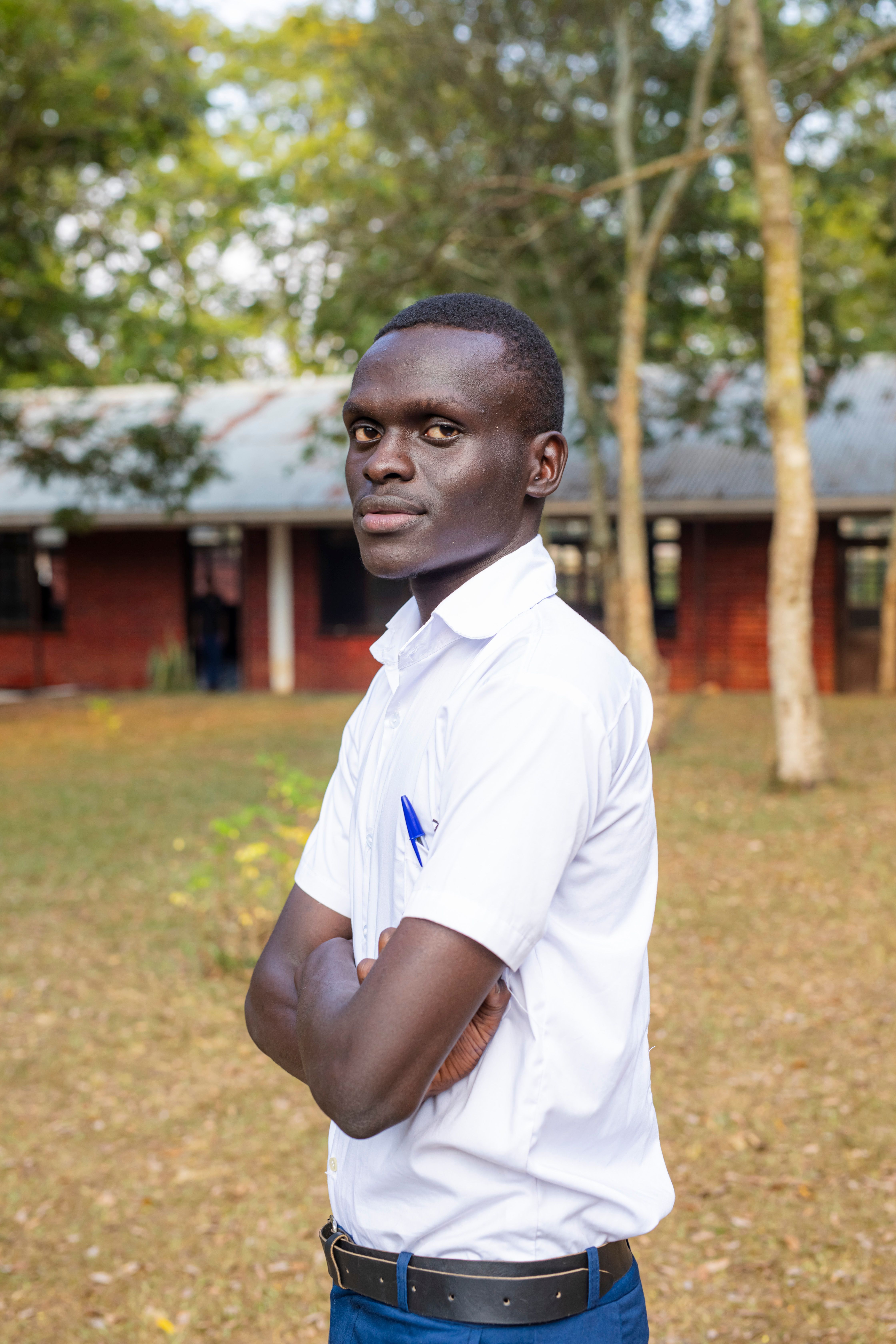 Man standing confidently outdoors with arms crossed, wearing a white shirt. Natural background setting.