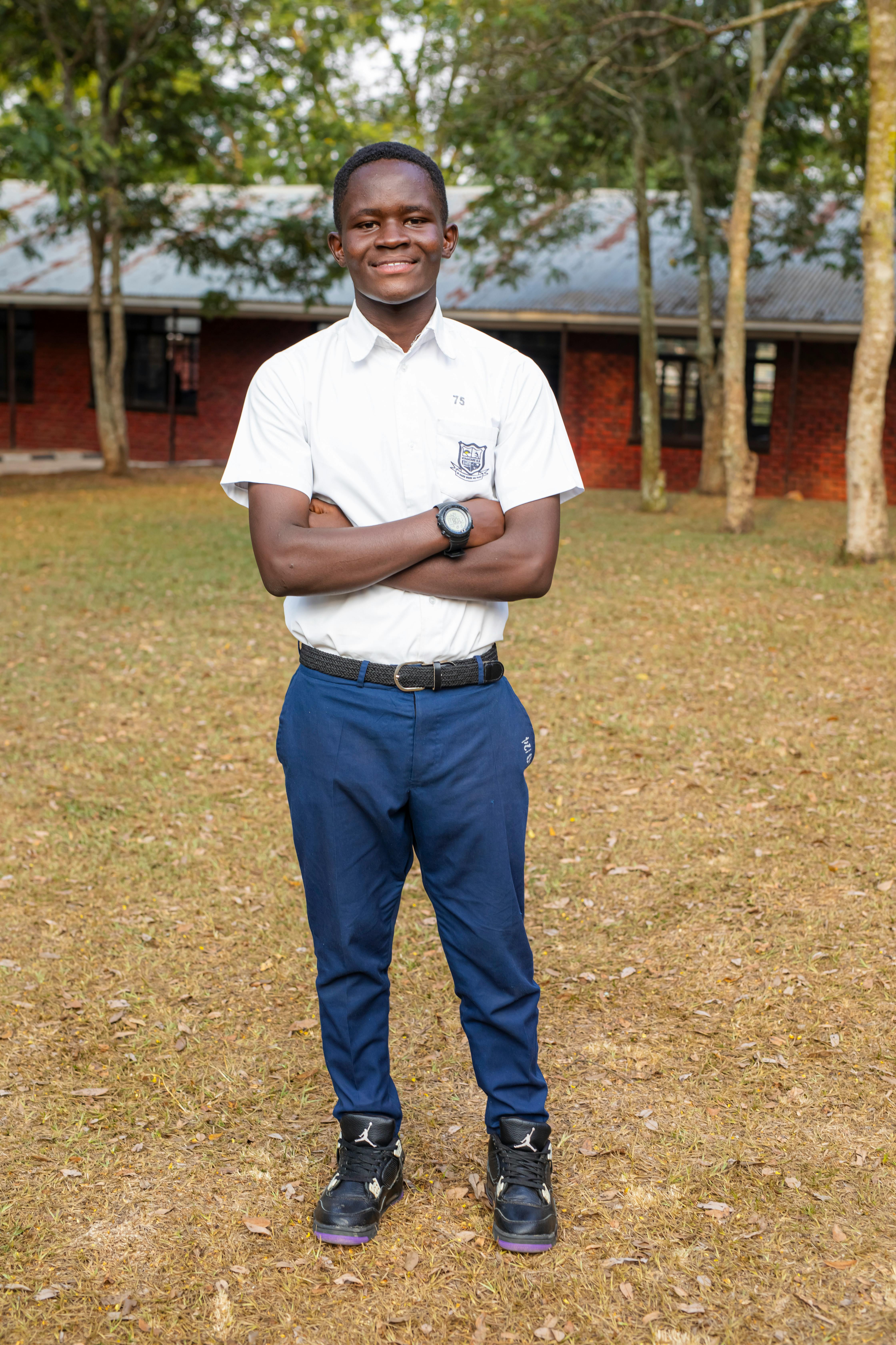 Portrait of a smiling student standing outdoors with a school building in the background.