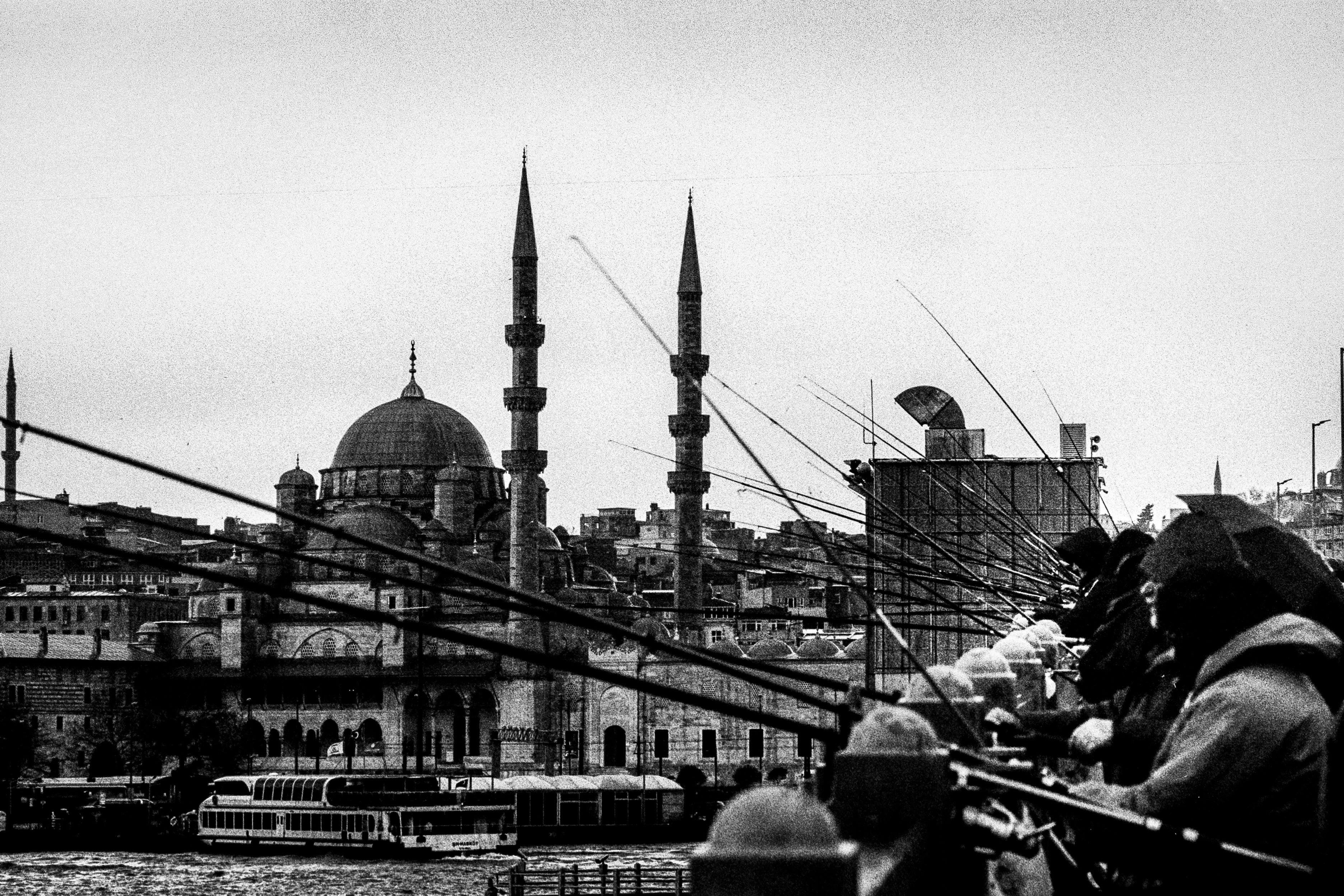 Black and white view of a mosque and fishermen on Galata Bridge in Istanbul.