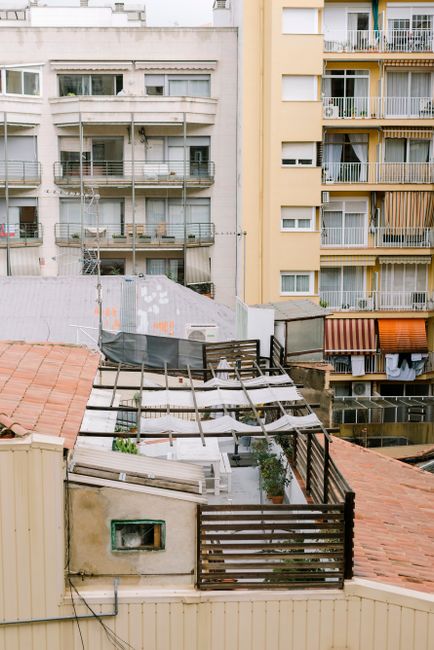 A rooftop terrace in a city with potted plants and urban residential buildings in the background.