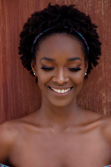 Portrait of a smiling woman with afro hairstyle and nose ring, standing against a wooden background in Angola.