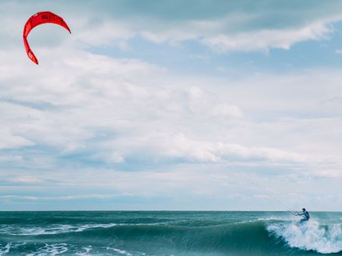 Free Exciting kitesurfing scene at Palavas-les-Flots with vibrant red kite and ocean waves. Stock Photo
