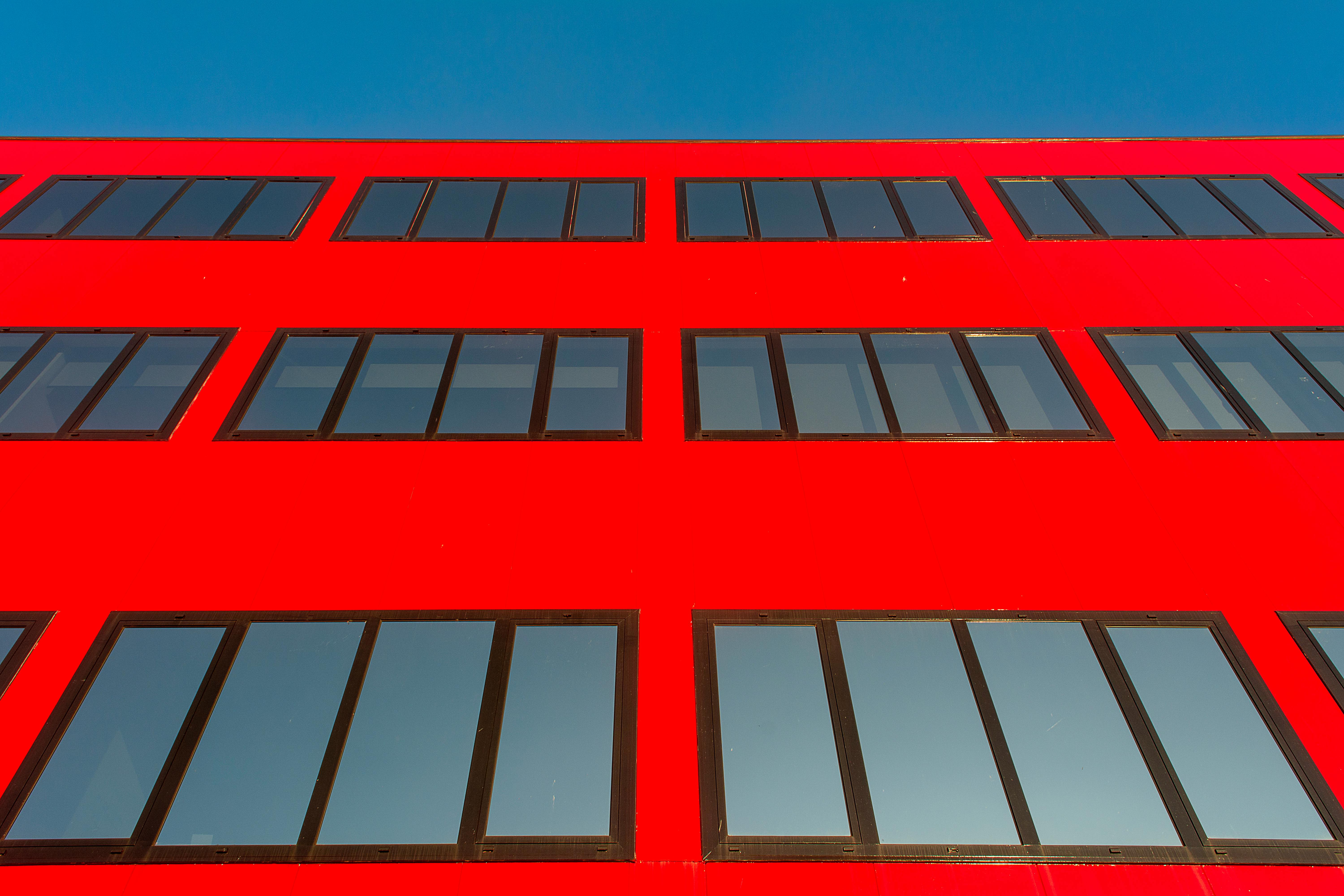 Bright red building facade with reflective windows against a clear blue sky, showcasing modern architecture.