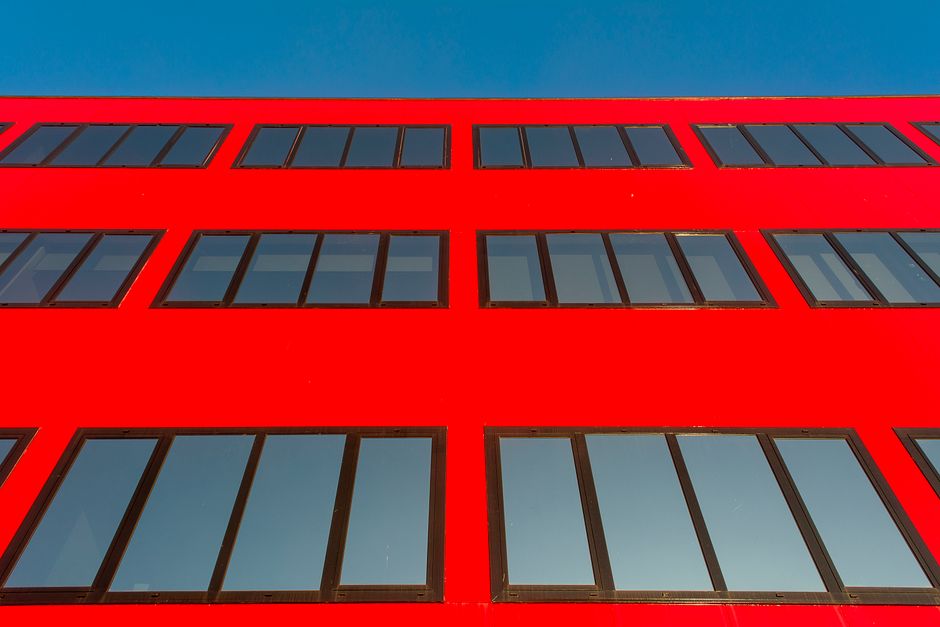 Bright red building facade with reflective windows against a clear blue sky, showcasing modern architecture.