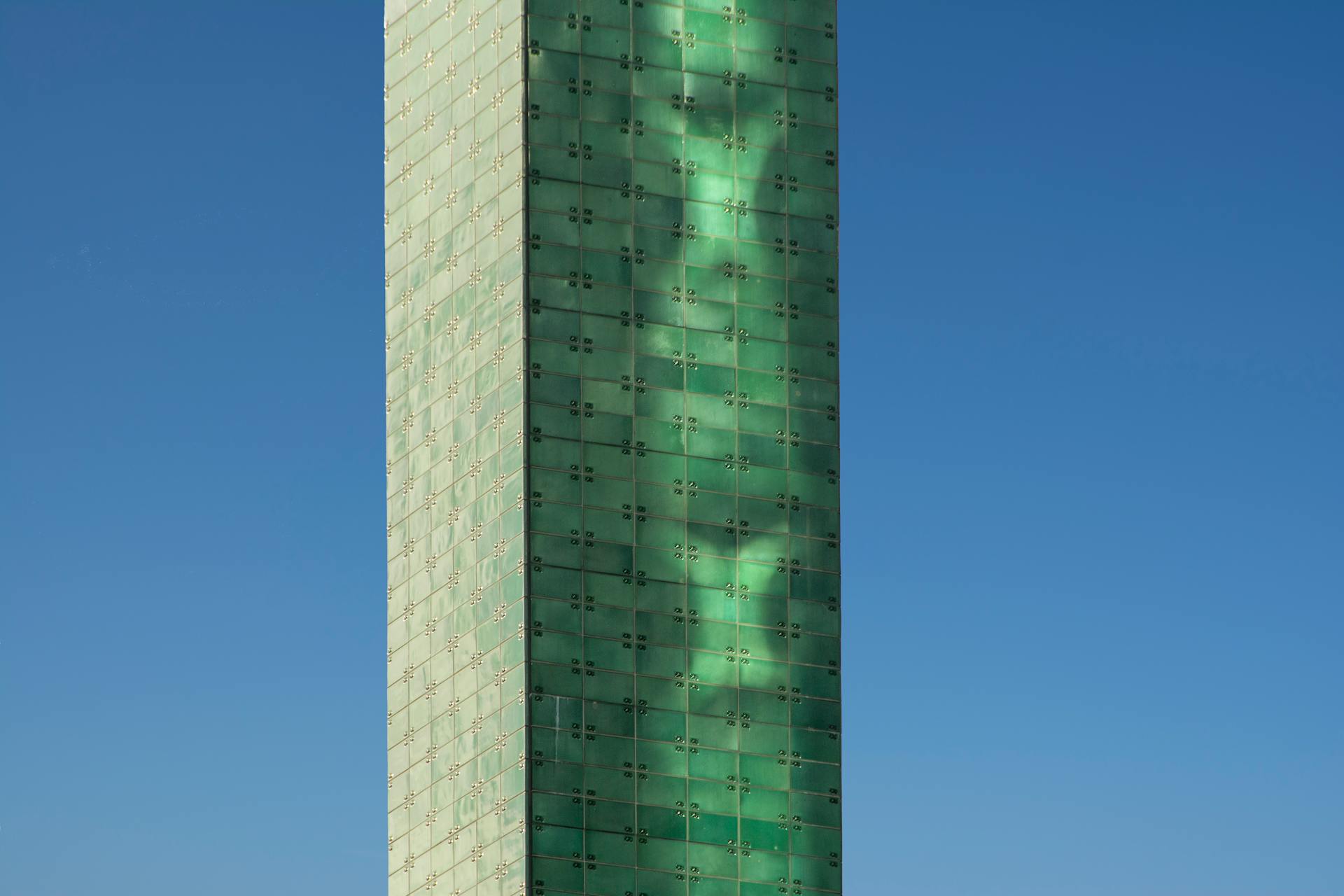 A modern glass tower with a unique design contrasting against a clear blue sky.