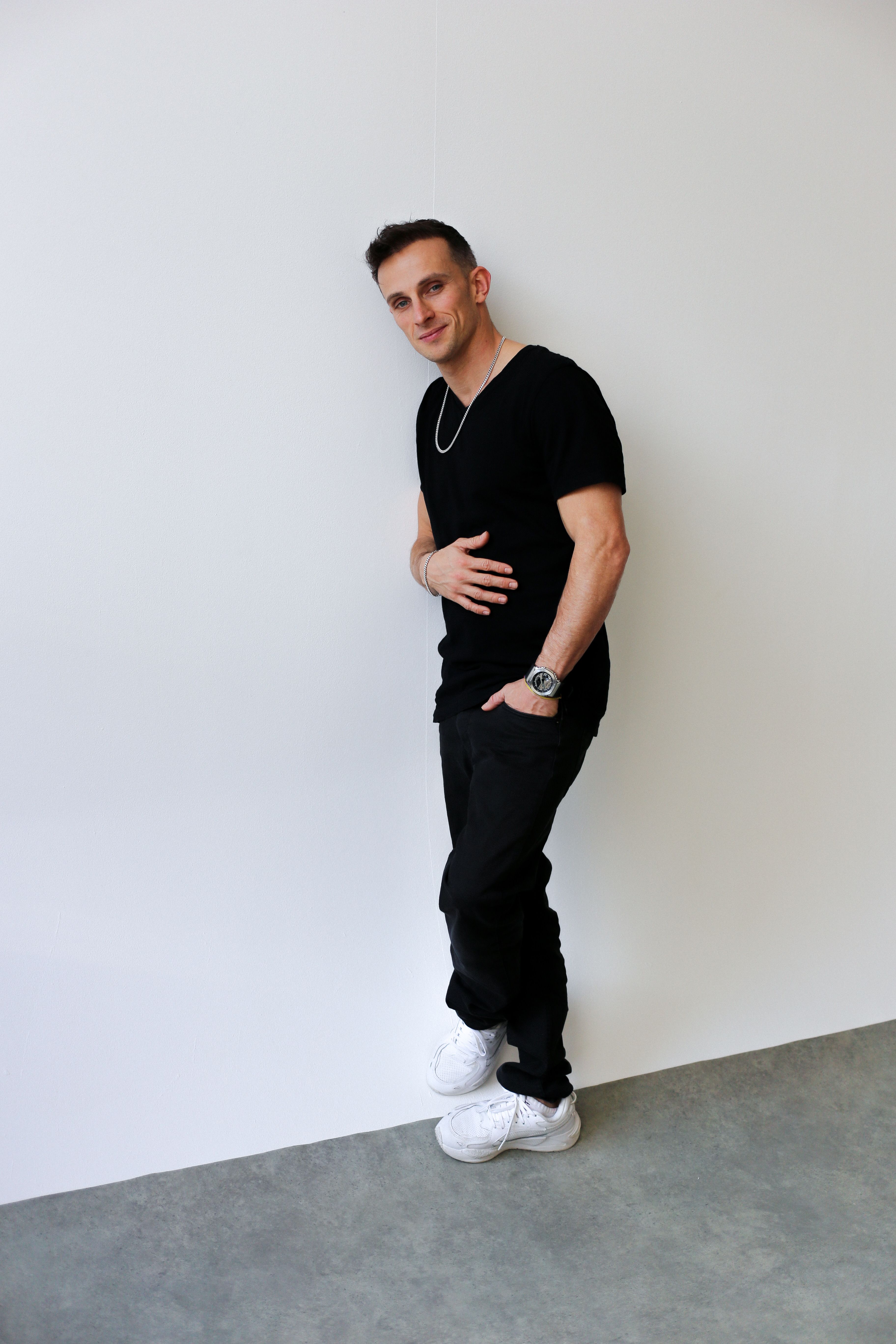 A stylish male model posing against a white wall in Berlin, showcasing modern fashion with a minimalist vibe.