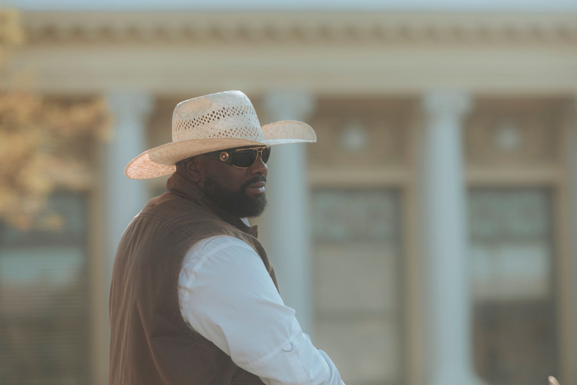 A fashionable man in sunglasses and cowboy hat standing outside a classical building.