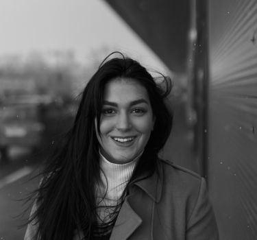 A smiling woman with long hair in a black and white portrait outdoors.