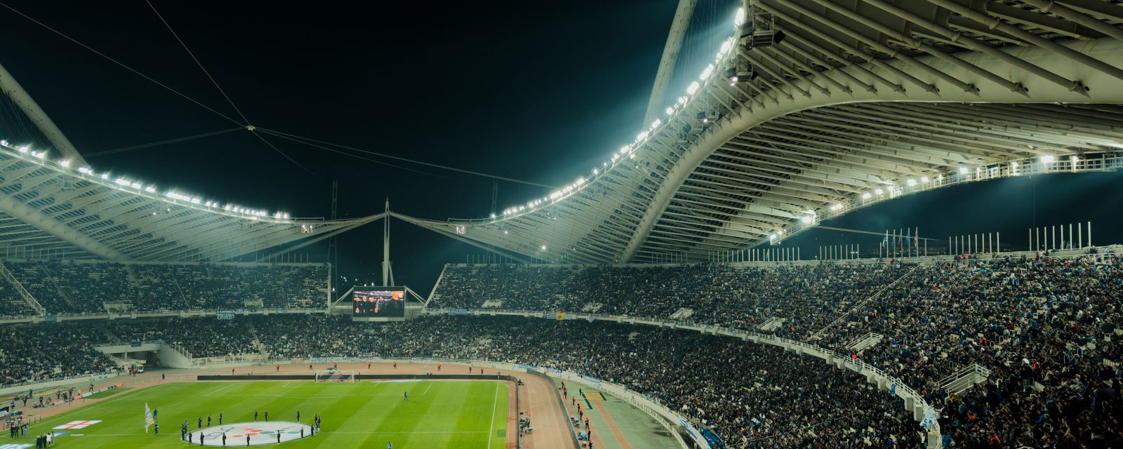 Floodlit football stadium at night packed with fans