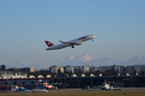 Free A Swiss airplane takes off at Geneva Airport with the Alps in the background. Stock Photo