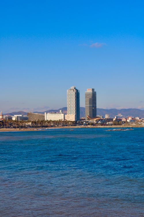 Free View of Barcelona's skyline featuring the iconic Mapfre Tower and Hotel Arts near the coast. Stock Photo