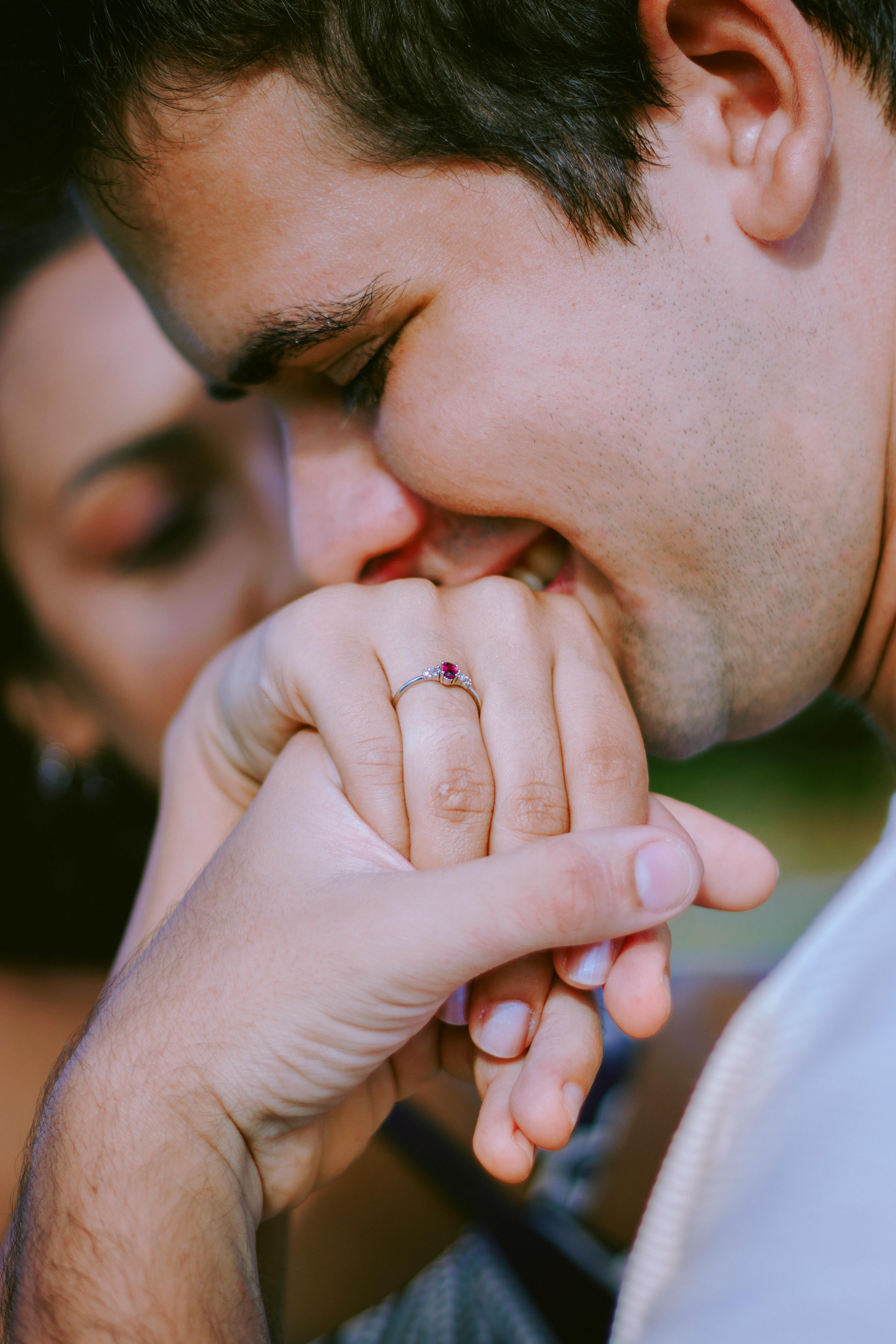 Close-up of a man kissing a woman's hand with an engagement ring, symbolizing romance and love.