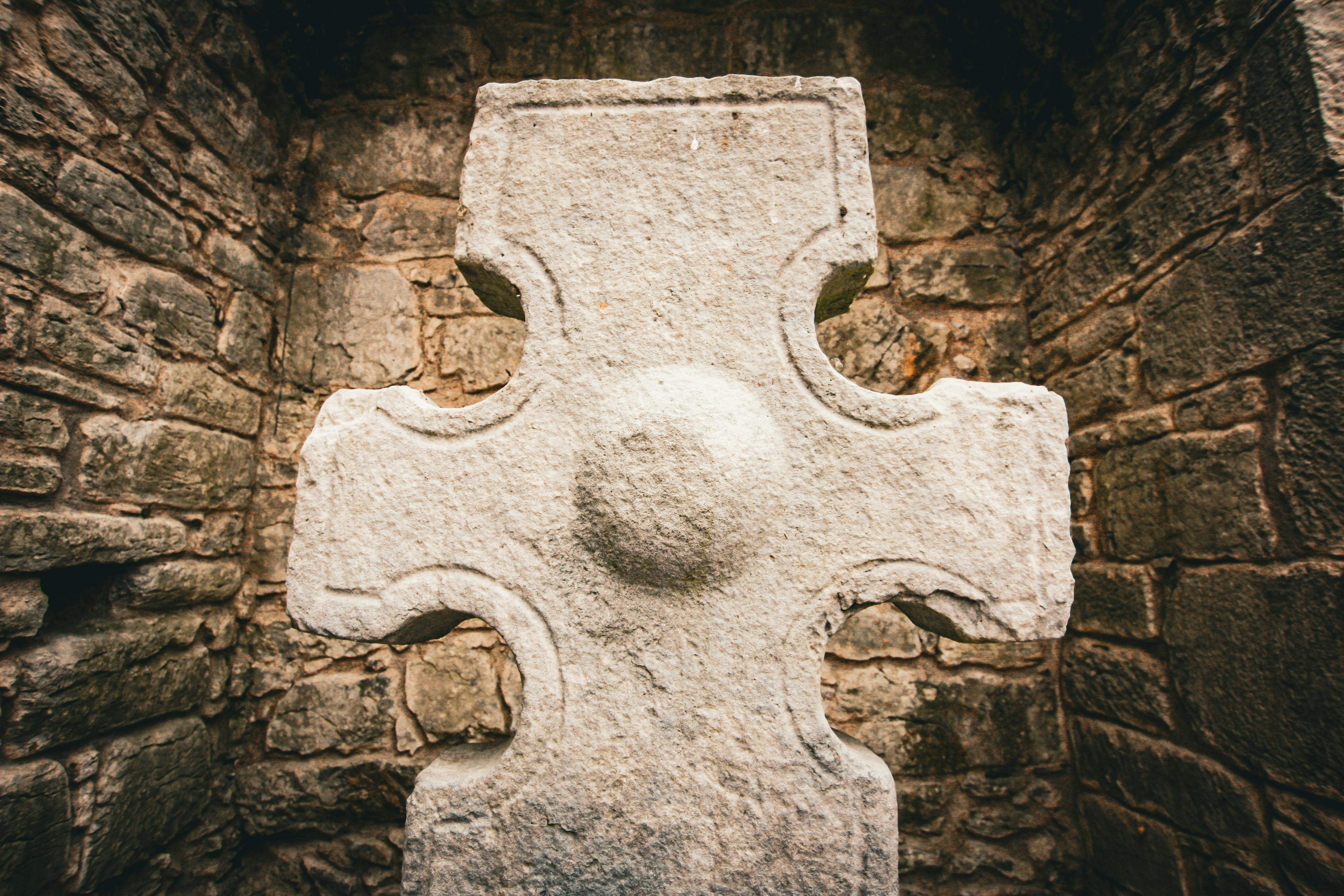 Close-up of a Celtic stone cross within ancient stone walls, exuding historical charm.