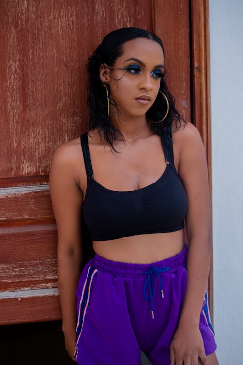 Photo of Woman in Black Sports Bra and Purple Shorts Posing by Wooden Door