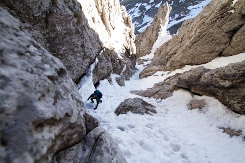 Человек идет между скалой горы со снегом