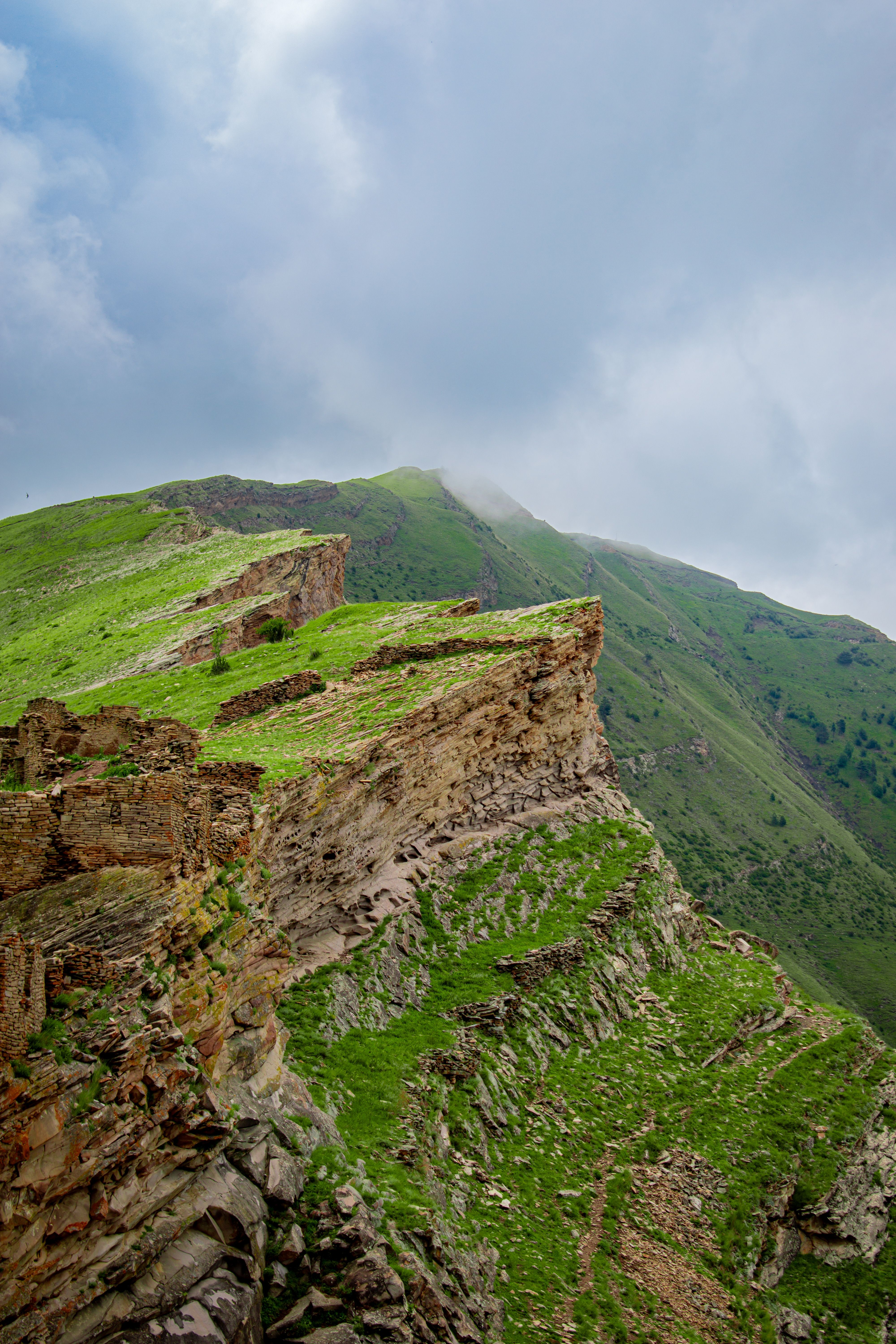 Breathtaking view of a steep mountain cliff covered in vibrant green grass under a cloudy sky.
