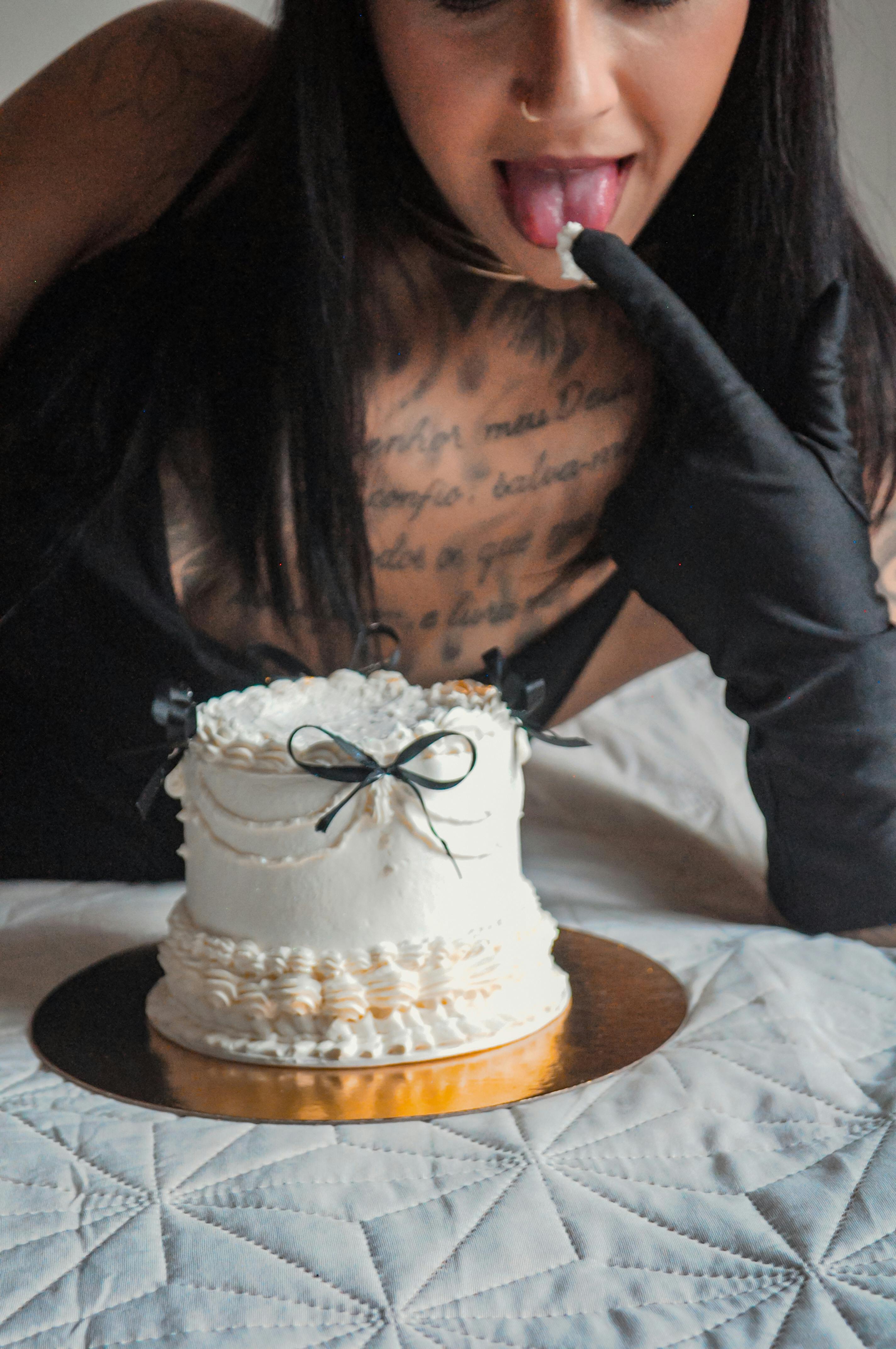 Elegant woman tastes cake icing while wearing black gloves.
