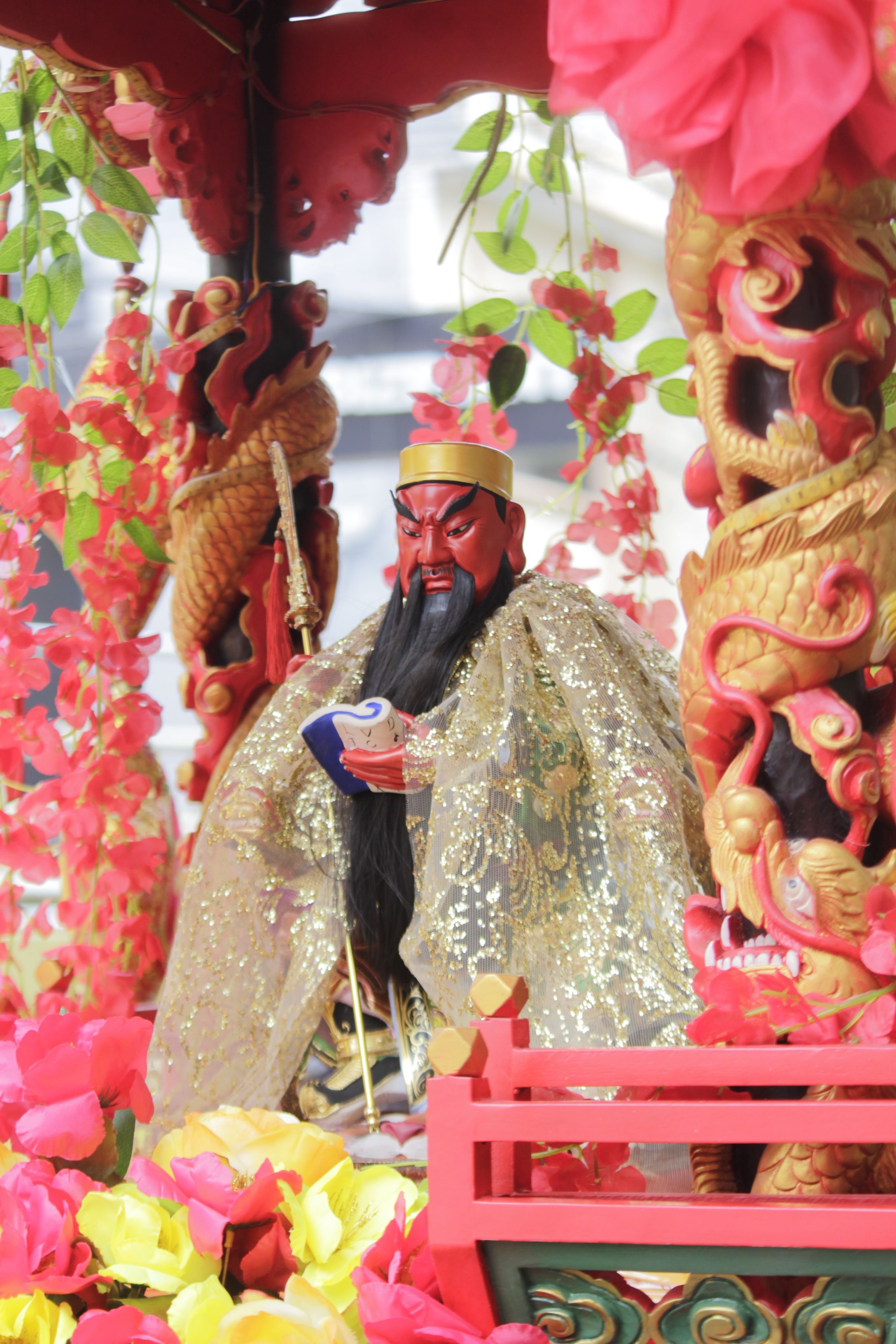 Colorful Chinese statue adorned with flowers at Makassar festival.