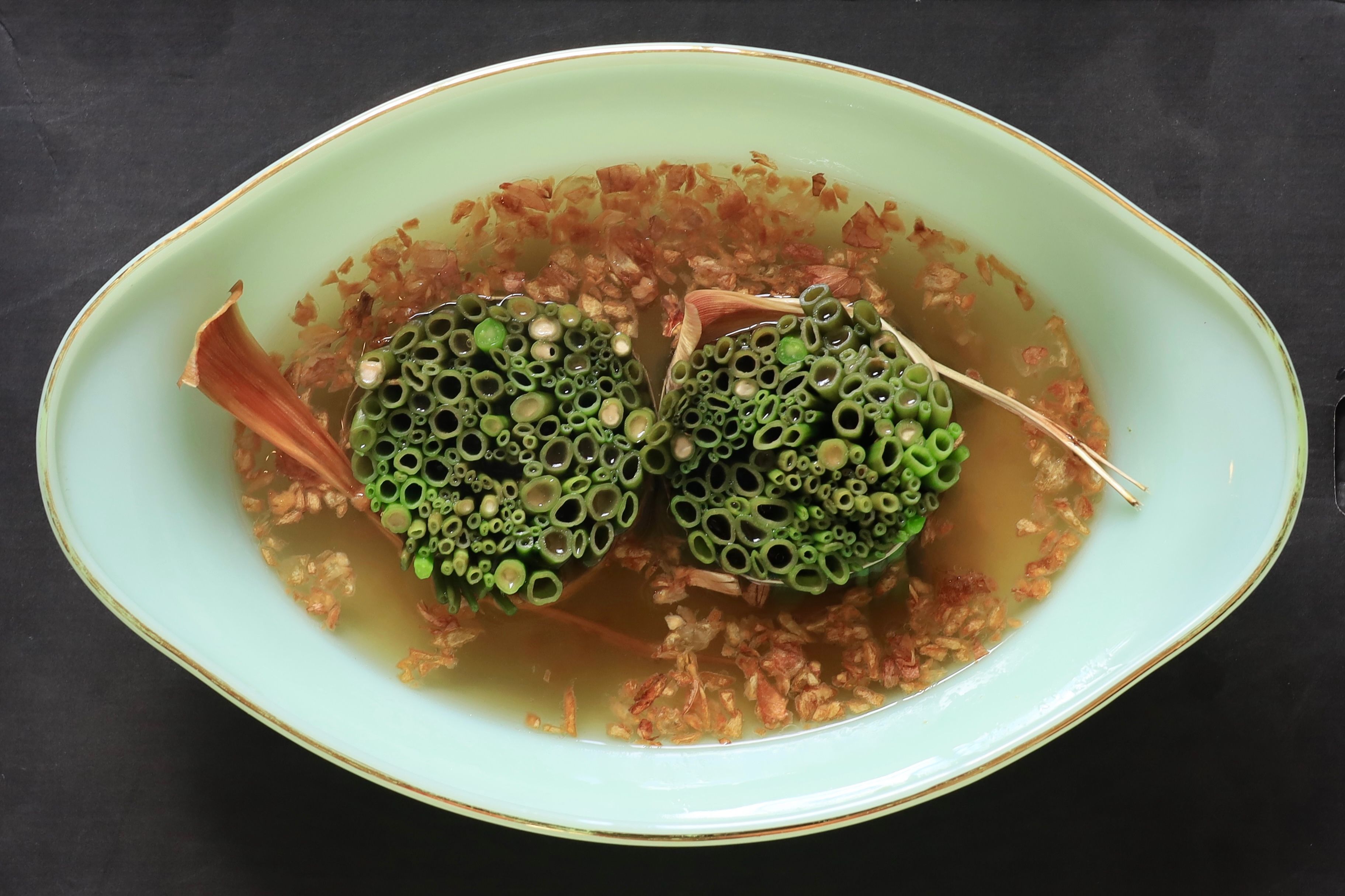 Green lotus pods floating in an abstract dish with an organic, artistic presentation.