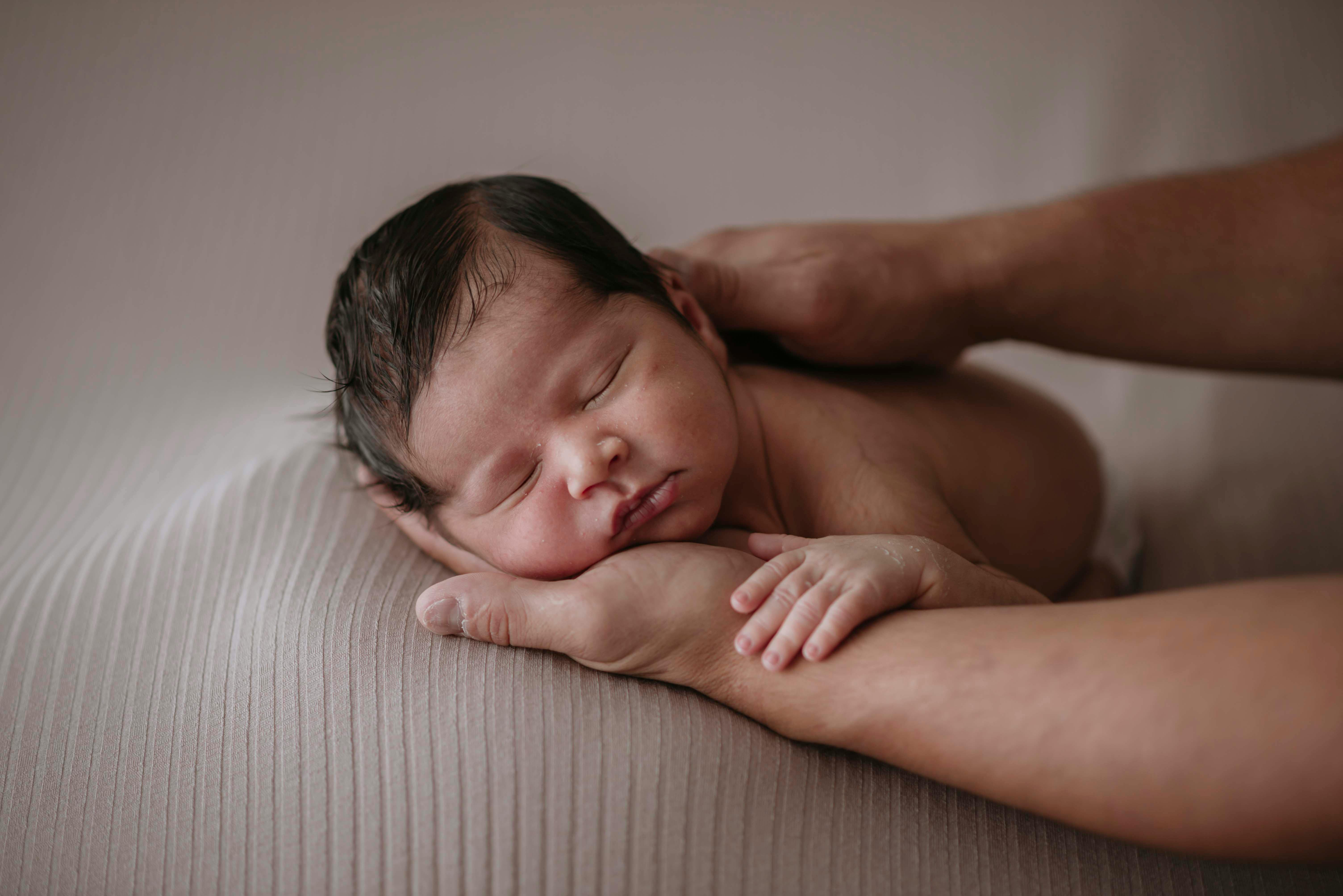 A serene newborn baby sleeping on supportive hands, conveying warmth and tenderness.