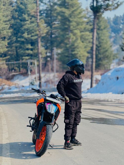 Free Biker in protective gear stands beside a sports motorbike on a snowy forest road. Stock Photo