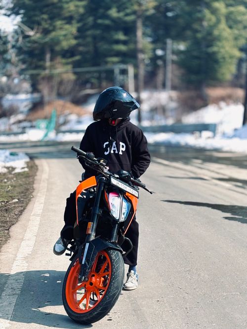 Free Biker on a vibrant orange motorcycle on a snowy road with forested backdrop. Stock Photo