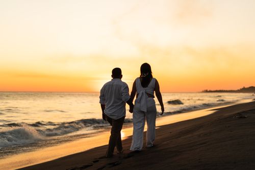 Free Couple walking hand in hand on a beach during a romantic sunset. Stock Photo