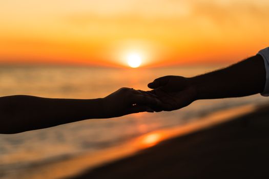 Silhouette of a couple holding hands during a romantic beach sunset.