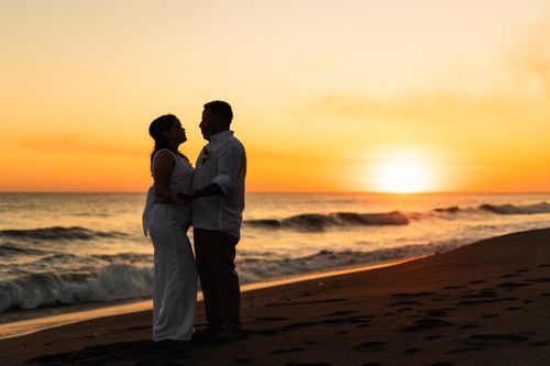 Free A romantic silhouette of a couple embracing on a beach during sunset. Stock Photo