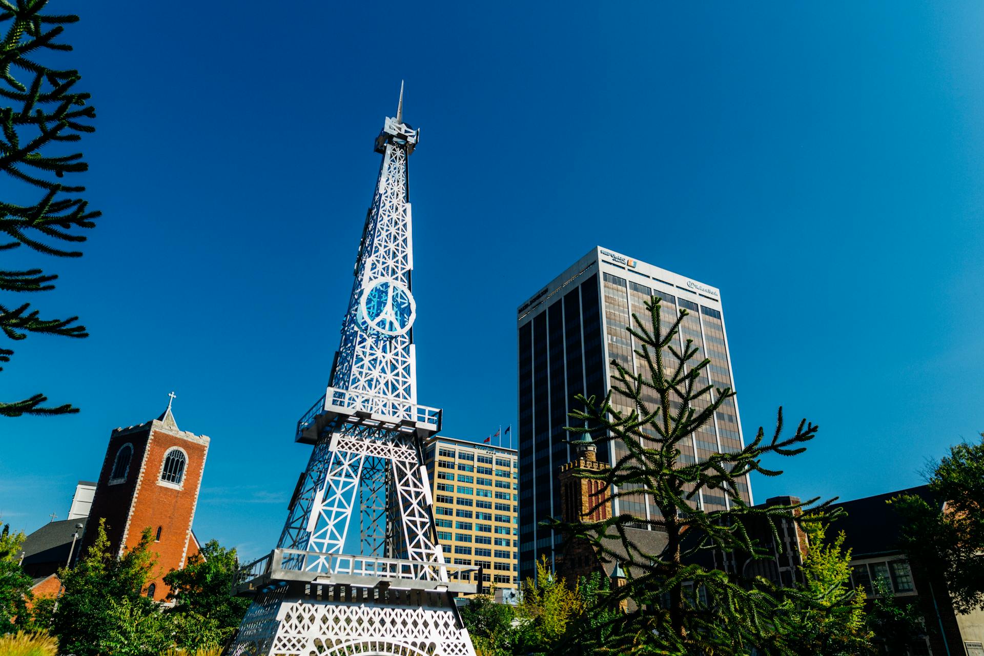 A striking replica tower among city buildings and a church under a clear blue sky.