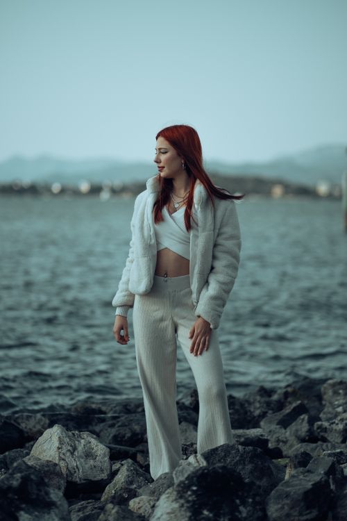 Free Fashionable woman with red hair at a rocky coastline wearing white attire. Stock Photo
