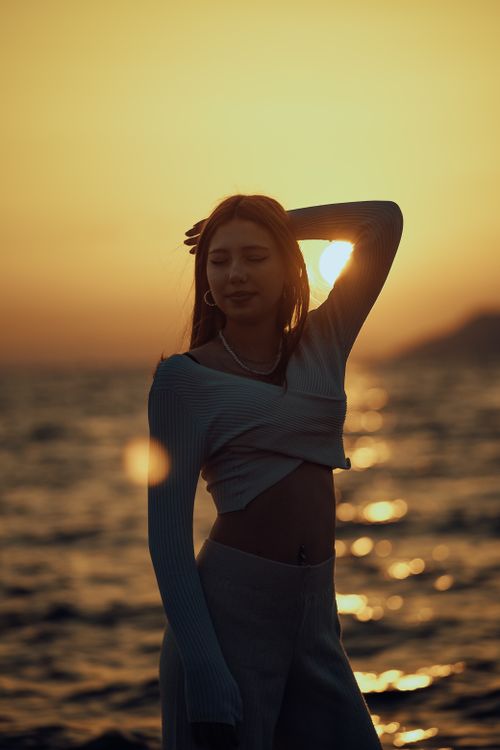 Free Silhouette of a woman posing gracefully by the sea at sunset. Stock Photo