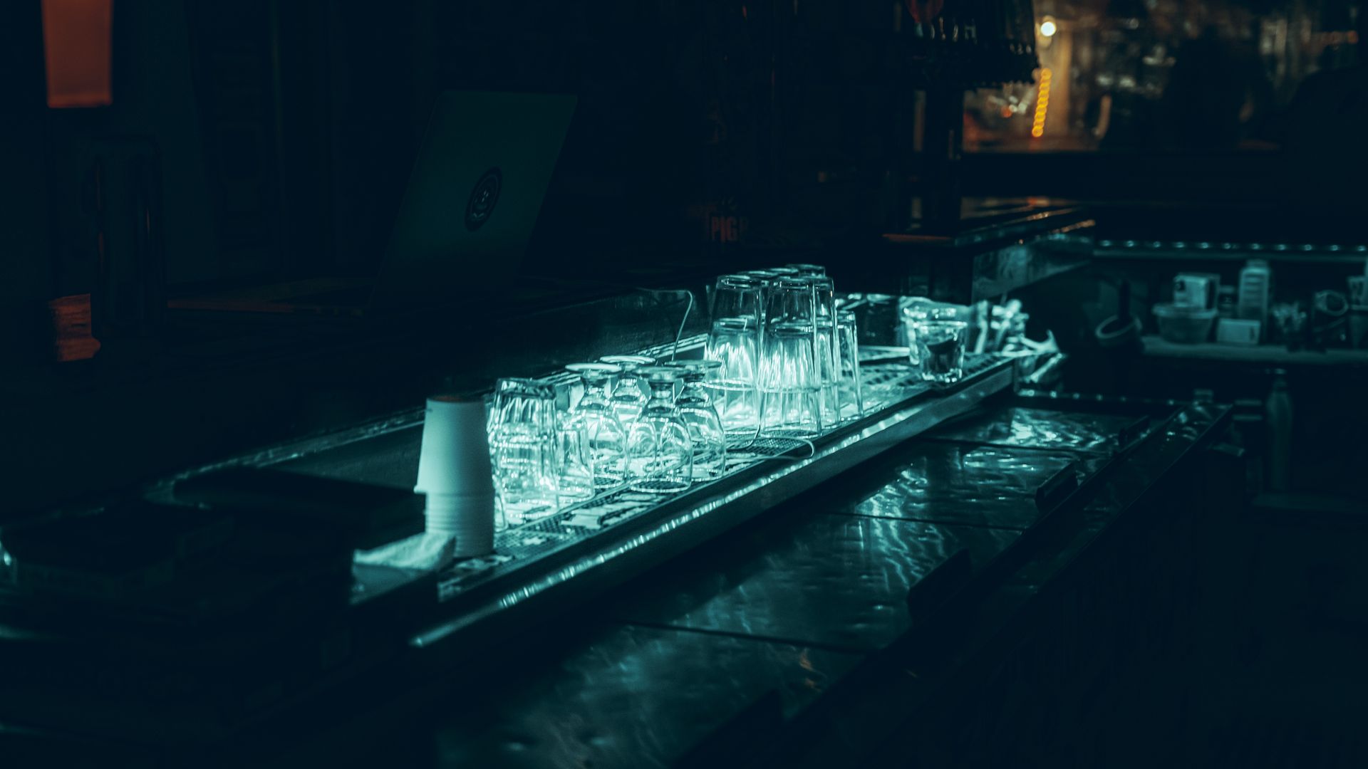 Vasos vacíos alineados sobre la barra de un bar con luz tenue